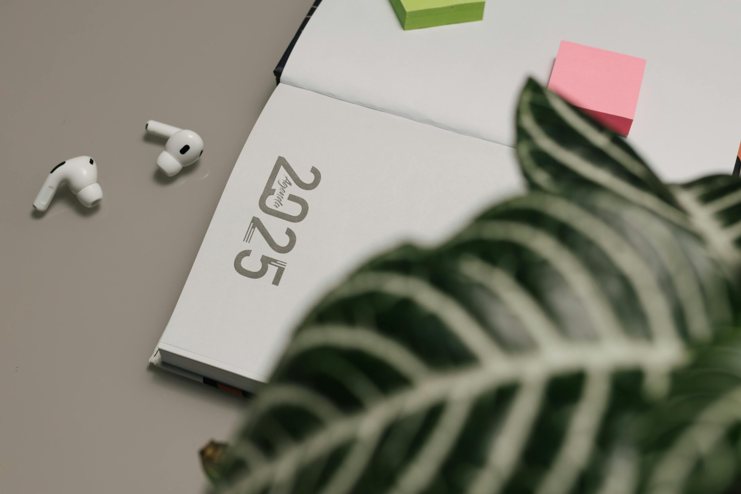 Open 2025 planner with AirPods and sticky notes, creating a modern workspace vibe.